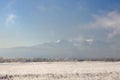 Winter landscape with snowy mountains behind field covered with frozen dry grass under dark blue sky during sunrise Royalty Free Stock Photo