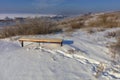 Winter landscape, sunny day. Footprints in the fresh snow lead to a wooden bench that stands on the high bank of the river Royalty Free Stock Photo