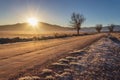 Winter landscape at sunrise with the sun rising between the mountains and icy road towards the horizon Royalty Free Stock Photo