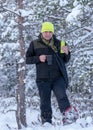 Winter landscape from the swamp, a man drinking tea from a thermos, walking in snowshoes, snow-covered pines in the background,