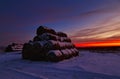 Winter landscape with view of snow-covered straw bales in field at sunset Royalty Free Stock Photo