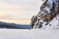 Winter landscape with a wide frozen river in a snowy wooded valley with high cliffs Royalty Free Stock Photo