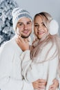 Winter love story with couple weared fur headphones, hats, white sweaters. Happy young couple hugs and kiss near