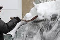 Winter. A man with a metal shovel cleans car from snow on the street after big snowstorm in the city, all cars under snow, icy roa Royalty Free Stock Photo