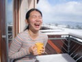 Winter morning coffee - young happy and attractive Asian Japanese woman at hotel or home balcony in the snow drinking coffee Royalty Free Stock Photo