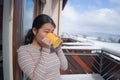 Winter morning coffee - young happy and attractive Asian Japanese woman at hotel or home balcony in the snow drinking coffee Royalty Free Stock Photo