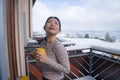 Winter morning coffee - young happy and attractive Asian Korean woman at hotel or home balcony in the snow drinking coffee looking Royalty Free Stock Photo