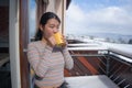 Winter morning coffee - young happy and attractive Asian Korean woman at hotel or home balcony in the snow drinking coffee looking Royalty Free Stock Photo