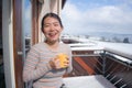 Winter morning coffee - young happy and attractive Asian Korean woman at hotel or home balcony in the snow drinking coffee looking Royalty Free Stock Photo