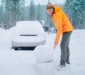 Winter morning routine. Smiling man with a shovel removing snow from the path and cleaning auto. Car covered with snow as a huge Royalty Free Stock Photo