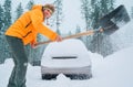 Winter morning routine. Smiling man with a shovel removing snow from the path and cleaning auto. Car covered with snow as a huge Royalty Free Stock Photo