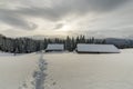 Winter mountain landscape. Old wooden houses on snowy clearing on background of mountain ridge, spruce forest and cloudy sky. Royalty Free Stock Photo