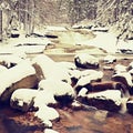 Winter at mountain river. Big stones in stream covered with fresh powder snow and lazy water with low level.