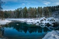 Winter panorama, small turquoise lake in the mountains among snow-covered forest. Trees are reflected in the lake water. Majestic Royalty Free Stock Photo