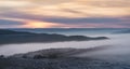 Winter panorama at sunset with snow covered hills with low fog in the valley and cloud cover Royalty Free Stock Photo