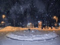 Winter park at night. Snowfall and orange light lanterns.