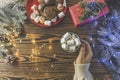 Winter party concept with hot chocolate, hands with cocoa cup with marshmallow on wooden table with christmas decorations, top