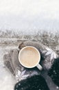 Winter picture: hands in knitted gray gloves holding a Cup of hot coffee on a snowy day on a wooden rustic background in the