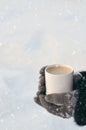 Winter picture: hands in knitted gray gloves holding a Cup of hot coffee on a snowy day on a wooden rustic background in the