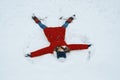 Winter portrait of cheerful girl having fun in the snow, lying on the snow in the form of angel, top view
