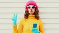 Winter portrait close up of woman with phone blowing red lips sending sweet air kiss wearing a pink hat, yellow sweater over white Royalty Free Stock Photo