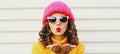 Winter portrait close up of young woman blowing red lips sending sweet air kiss wearing a pink hat, yellow sweater Royalty Free Stock Photo