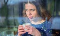 Winter portrait of happy beautiful young woman drinking coffee behind a window. Horizontal image Royalty Free Stock Photo