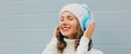 Winter portrait of happy smiling woman listening to music in headphones wearing a white hat, knitted sweater over blue Royalty Free Stock Photo