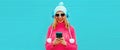 Winter portrait of happy smiling woman looking at smartphone in wireless headphones listening to music wearing pink knitted Royalty Free Stock Photo