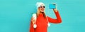 Winter portrait of happy smiling woman taking selfie with smartphone and coffee cup wearing red knitted sweater, white hat with Royalty Free Stock Photo