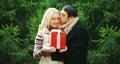 Winter portrait happy smiling young couple kissing with gift box outdoors on christmas tree background Royalty Free Stock Photo