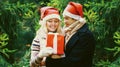 Winter portrait happy smiling young couple in santa hats with gift box outdoors on christmas tree background Royalty Free Stock Photo