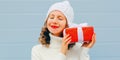 Winter portrait of happy young woman holding red gift box in her hands wearing a white knitted hat, sweater over blue Royalty Free Stock Photo