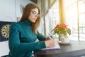 Winter portrait of student girl studying in cafe sitting with cup of coffee. Young woman writing in notebook using smartphone for Royalty Free Stock Photo