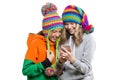 Winter portrait of two happy smiling pretty girls in knitted hats having fun with mobile phone, isolated on white background. Peop Royalty Free Stock Photo