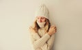 Winter portrait of woman freezing trying to warm up wearing warm soft knitted clothes, hat and sweater on beige studio background Royalty Free Stock Photo