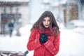 Winter portrait of young beautiful brunette woman wearing knitted snood and red coat covered in snow. Snowing winter beauty fashio