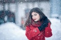 Winter portrait of young beautiful brunette woman wearing knitted snood and red coat covered in snow. Snowing winter beauty fashio