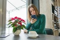 Winter portrait of young beautiful girl sitting at cafe with cup of coffee and mobile phone, snow outside the window, Christmas