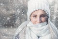 Winter portrait of young beautiful woman freezing and covering her face with woolen scarf on snowing winter day outdoors. Close-up Royalty Free Stock Photo