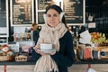 Winter portrait of young beautiful woman in knitted scarf, fur ears, warm sweater with cup of coffee. Girl standing near bar Royalty Free Stock Photo