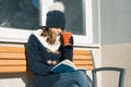 Winter portrait of young teen girl student in hat, warm clothes with cup of hot drink and book Royalty Free Stock Photo