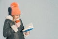 Winter portrait of young teen girl student in hat, warm clothes with cup of hot drink and book Royalty Free Stock Photo