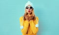 Winter portrait young woman blowing red lips sending sweet air kiss wearing yellow knitted sweater and white hat with pom pom Royalty Free Stock Photo