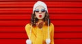 Winter portrait young woman blowing red lips sending sweet air kiss wearing yellow knitted sweater and white hat with pom pom Royalty Free Stock Photo