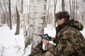 An employee of the national park in green camouflage clothes sets a camera trap on a tiger or leopard in a birch forest