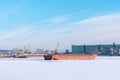 Winter river port. The barges are frozen in water, behind the barges there are loading cranes of yellow color