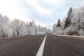 Winter road at frosty day with blue sky, landscape with snow covered trees, pattern of white highway dividing strip and ice on Royalty Free Stock Photo
