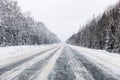 Winter road with ice on the asphalt, trees under snow during the winter frost