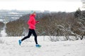 Winter running in park: happy active woman runner jogging in snow with Kyiv city skyline view, outdoor sport and fitness